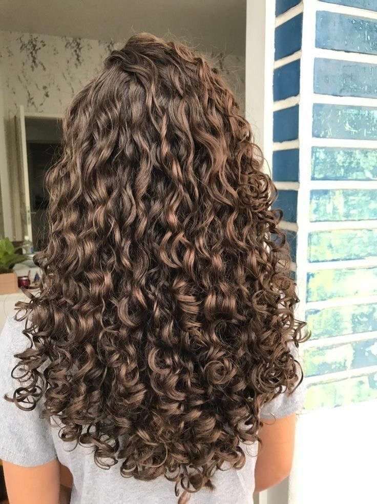 Visão de perfil de uma pessoa com cabelo cacheado, exibindo um corte em camadas elegante e cheio de volume.