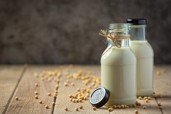 Garrafas de leite de soja com grãos ao redor em uma mesa de madeira, destacando opções de bebidas não lácteas.