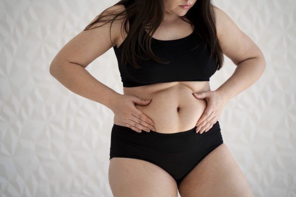 Perder Gordura Abdominal: Mulher jovem de frente, segurando sua barriga, simbolizando o foco na perda de gordura abdominal.