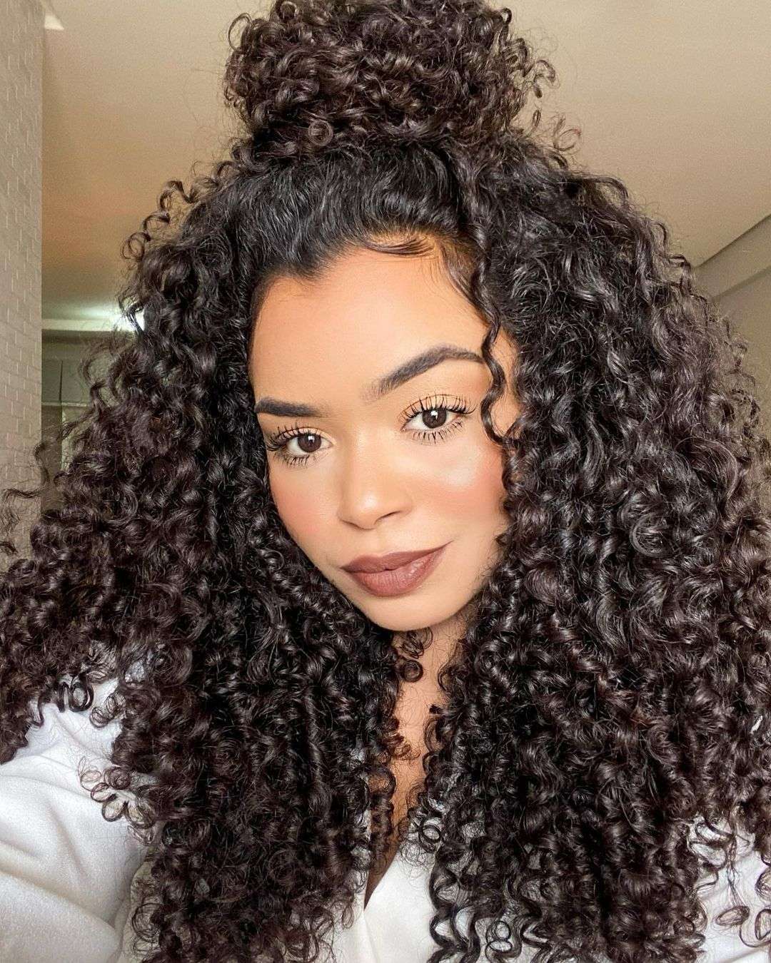 Half bun estiloso em cabelo cacheado, combinando cachos soltos com um coque despojado no topo da cabeça.