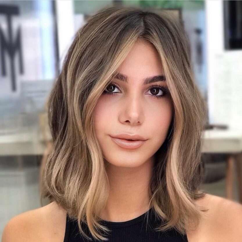 Loiro Tendência 2024: mulher com corte long bob em tom loiro cinza, radiante e moderno, contrastando com seu top preto.