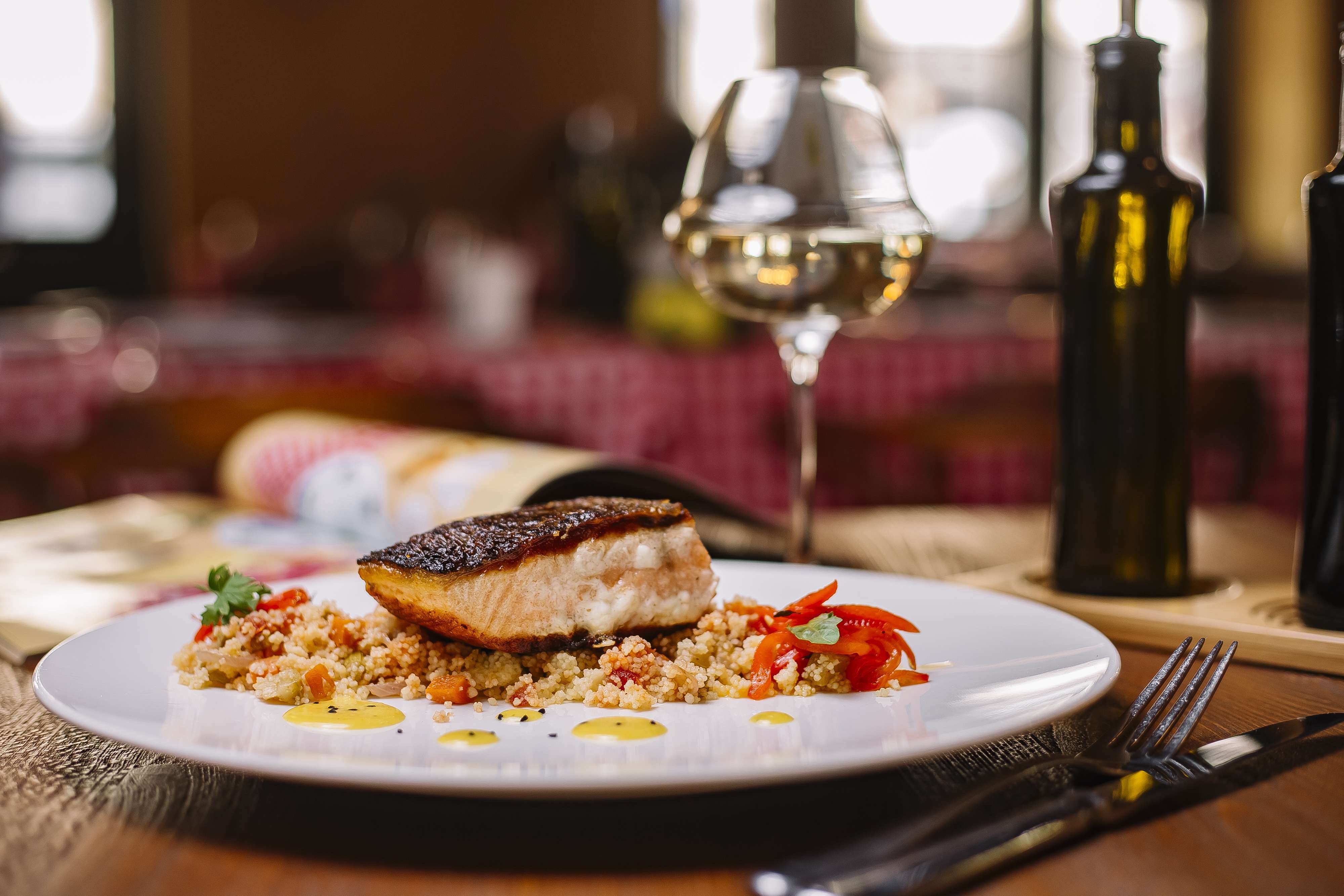 Tirar a Janta Ajuda a Emagrecer? Prato de jantar gourmet com filé de peixe grelhado sobre cuscuz marroquino, decorado com ervas e acompanhado de vinho branco.